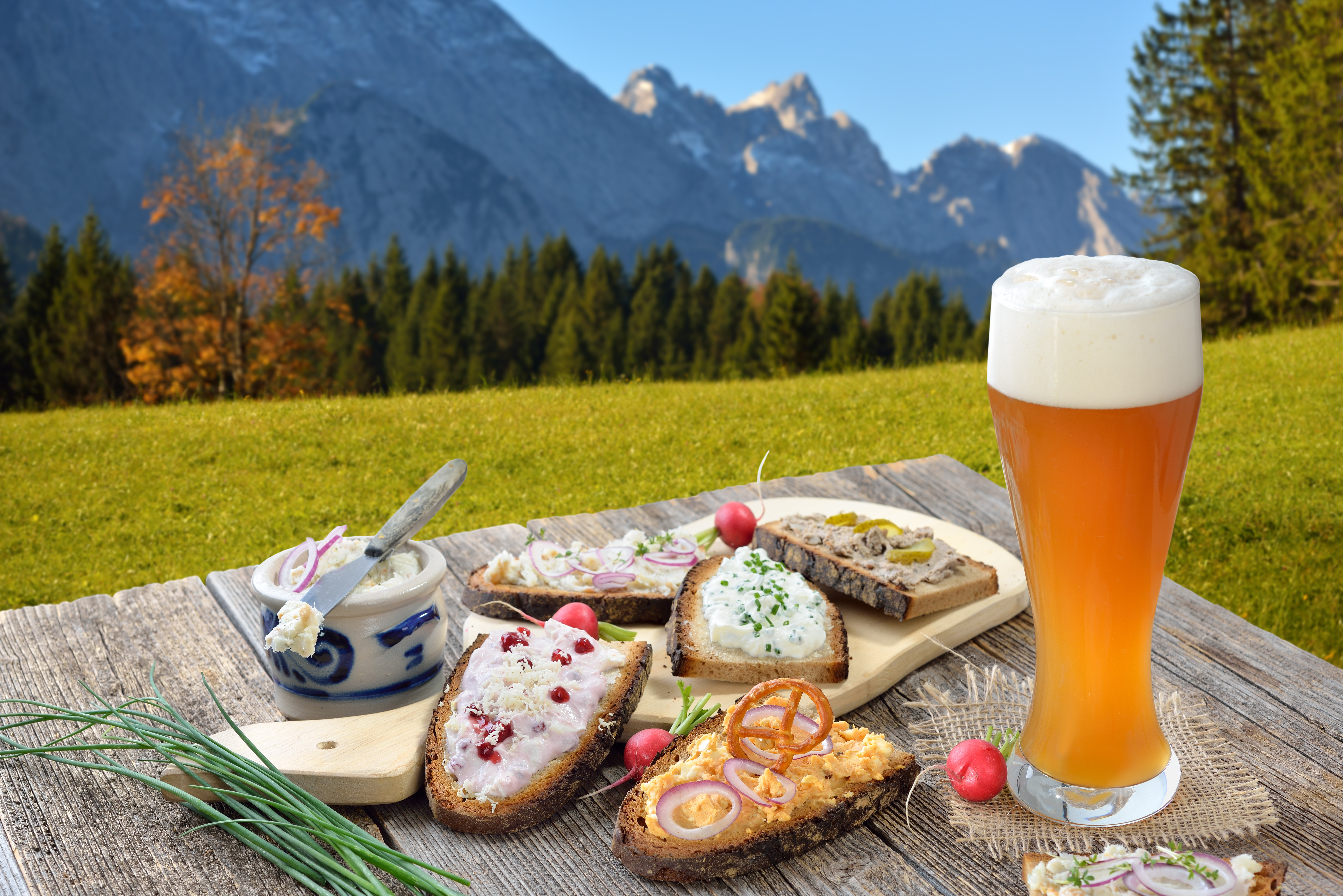 Hearty snack with different kinds of spreads on farmhouse bread served with a fresh yeast wheat beer on an old wooden table in the Bavarian Alps